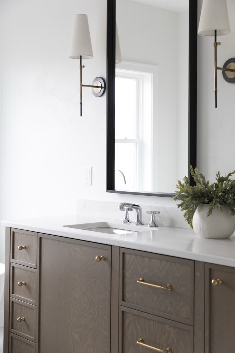 Bathroom vanity in dark stained wood with brass pulls and a black-framed mirror