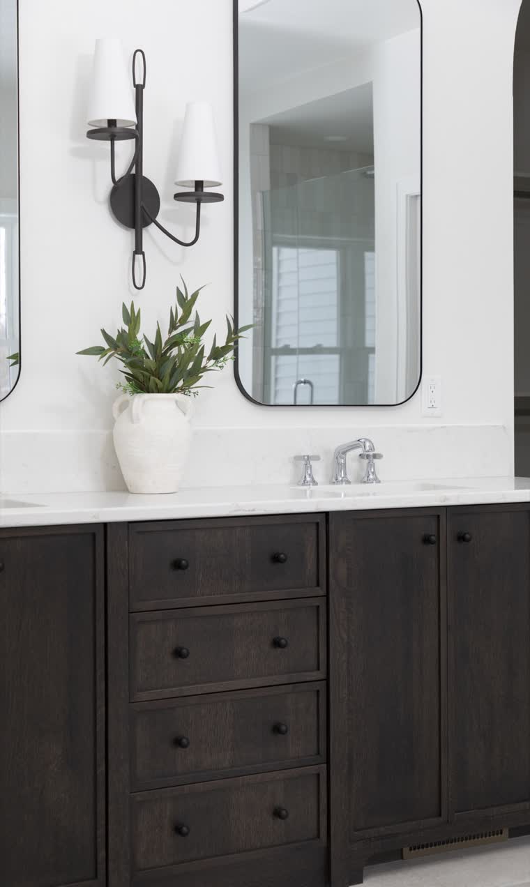 Dark wood vanity with a rounded mirror and a black wall sconce