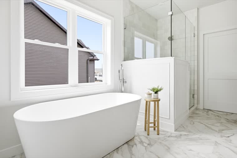 Primary bath with a freestanding tub under a large window and a glass shower
