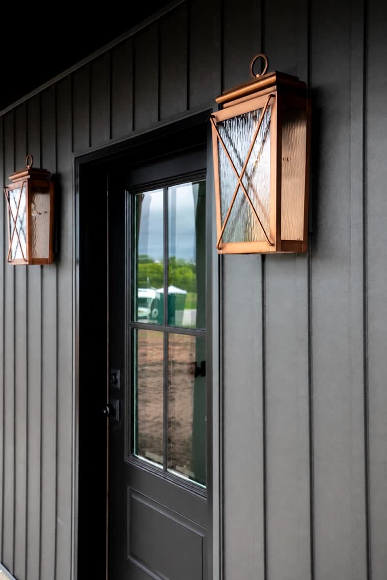 Close-up of a charcoal board-and-batten entry with copper lanterns