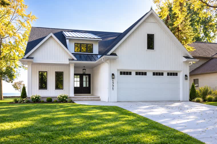 White two-story farmhouse-style home with a metal roof accent and a three-car garage