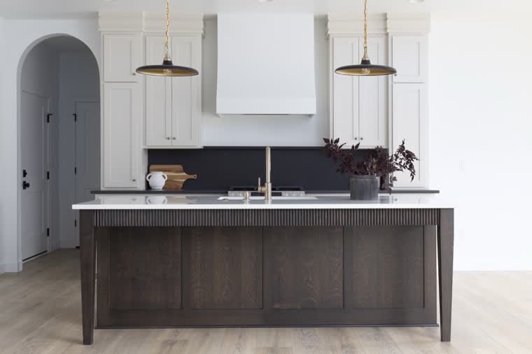 Kitchen with a dark wood island, white cabinets and brass pendant lights