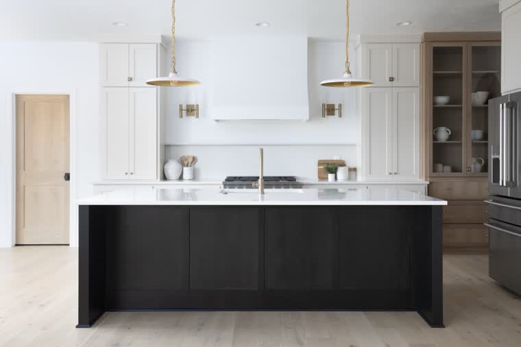White kitchen with a black island, brass pendants and an oak glass-front hutch