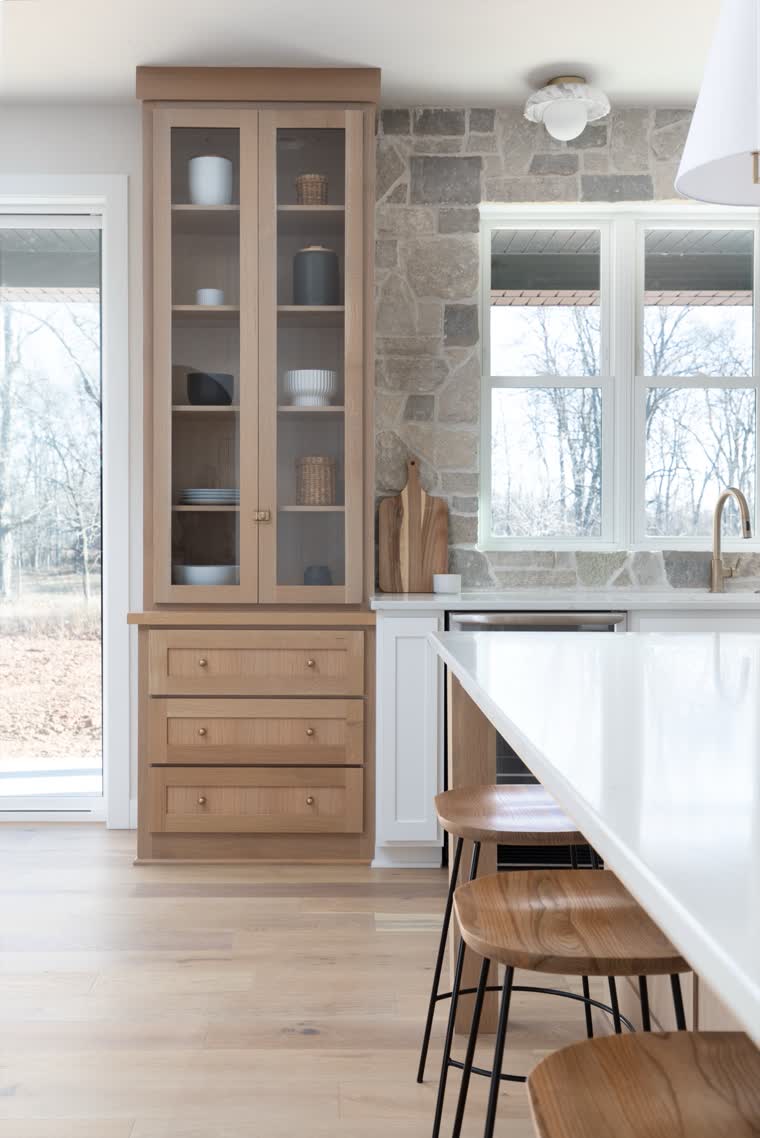 Oak glass-front cabinet beside a stone wall at the end of a kitchen island