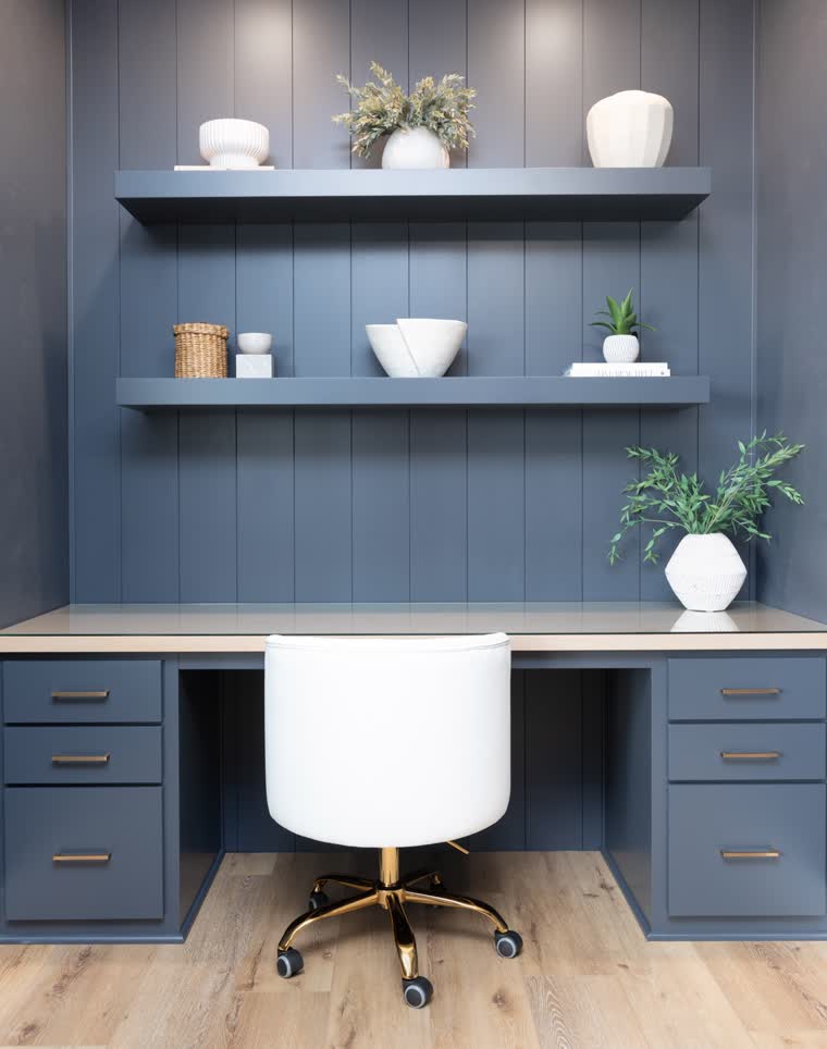 Home office nook with blue built-in cabinets, floating shelves and a white desk chair