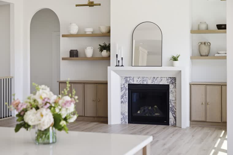 Living room with a marble-surround fireplace, floating shelves and oak cabinets on each side