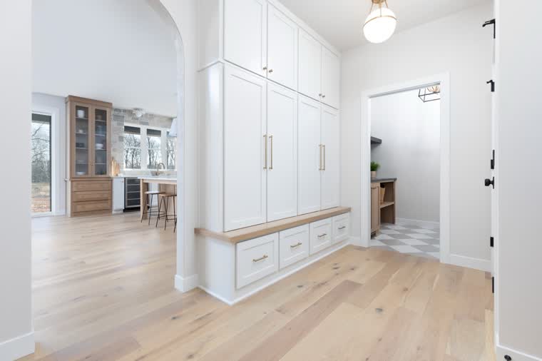 Mudroom with white floor-to-ceiling lockers and a bench, open to the kitchen