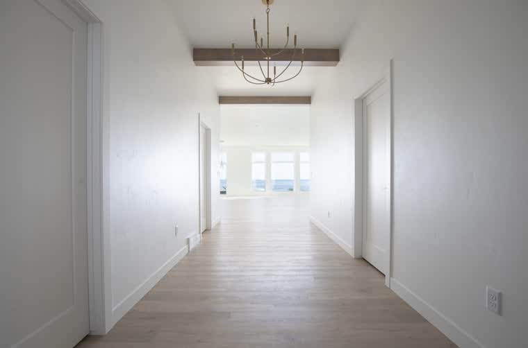 Wide hallway with a wood beam and a chandelier, looking toward the great room